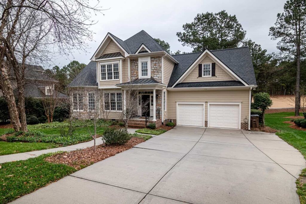 Suburban house with stone and siding exterior, two-car garage, and lush front yard.