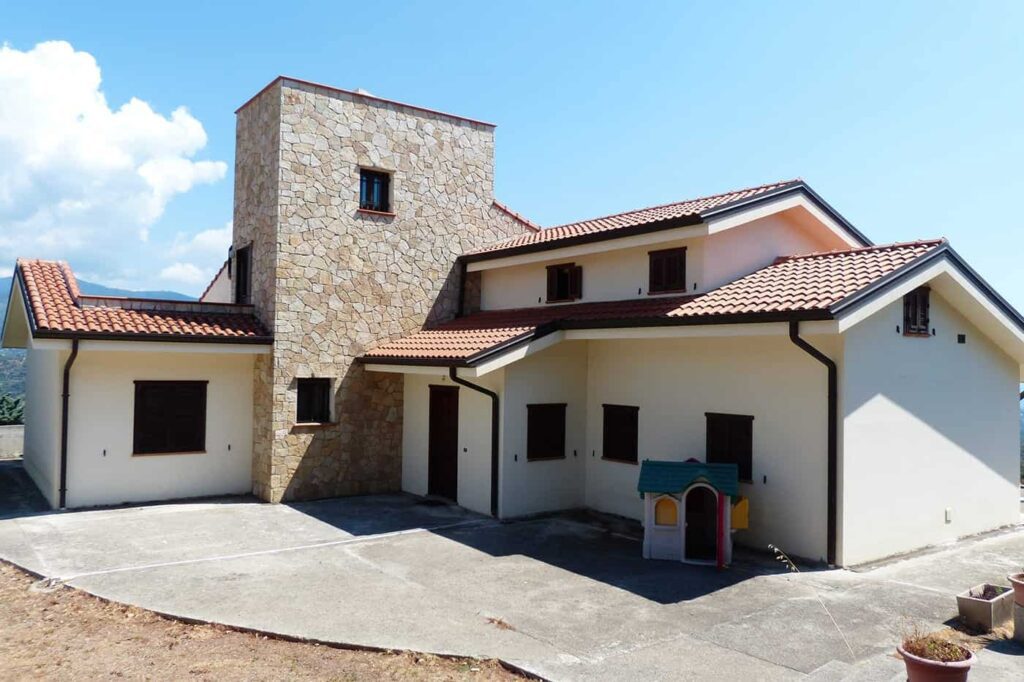 House with a stone tower, terracotta roof, and a playhouse in the front yard.