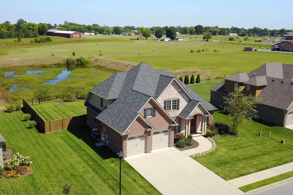 Aerial view of a large house with a brick and stone facade, grey roof, and a spacious yard.