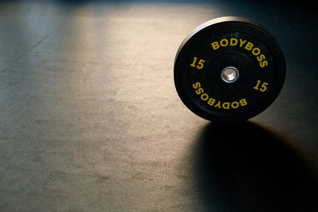 Black BodyBoss weight plate on gym floor, ideal for fitness and workout themes.