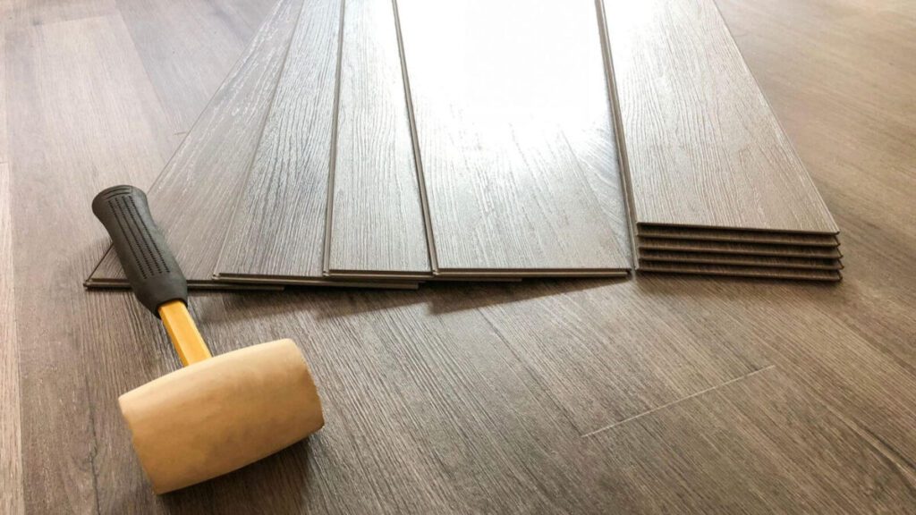 Close-up of wooden flooring planks stacked neatly, with a rubber mallet placed beside them, ready for installation.